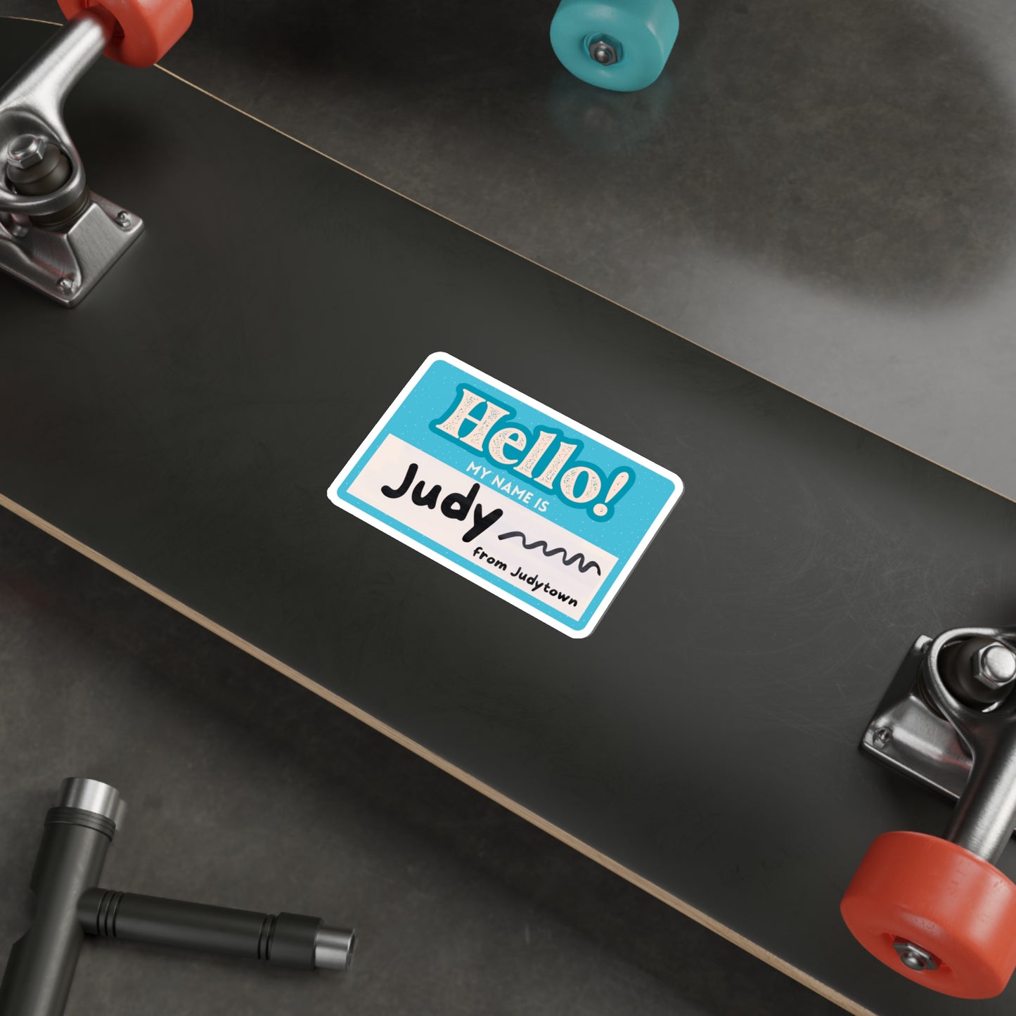 The back of a skateboard with a blue nametag sticker that says "Hello! My name is Judy from Judytown"