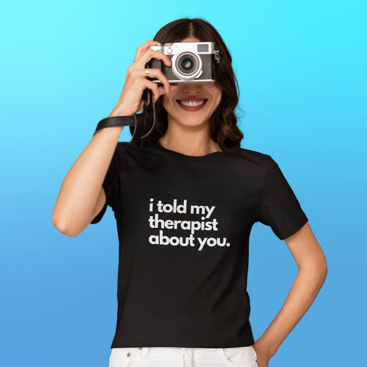 A person wearing a black t-shirt that reads “i told my therapist about you” in white font in the center.