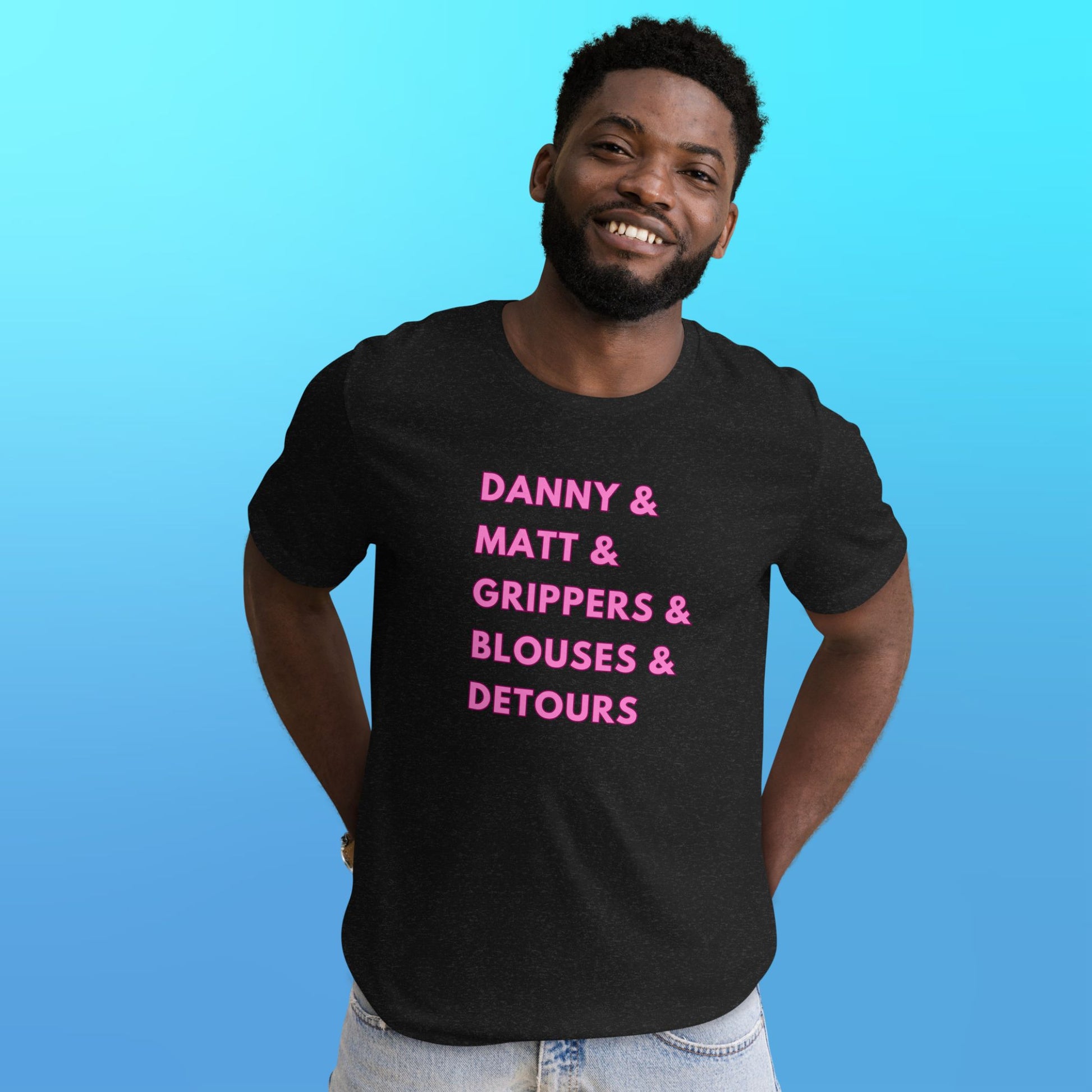 A person wearing a heather black T-shirt that reads "Danny & Matt & Grippers& Blouses & Detours" in pink capital letters