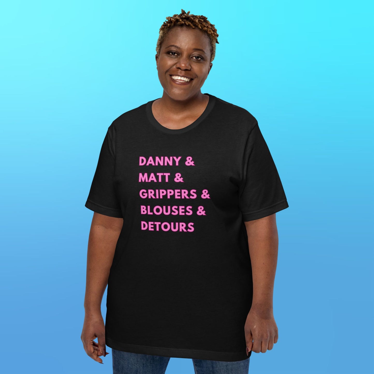 A person wearing a black T-shirt that reads "Danny & Matt & Grippers& Blouses & Detours" in pink capital letters