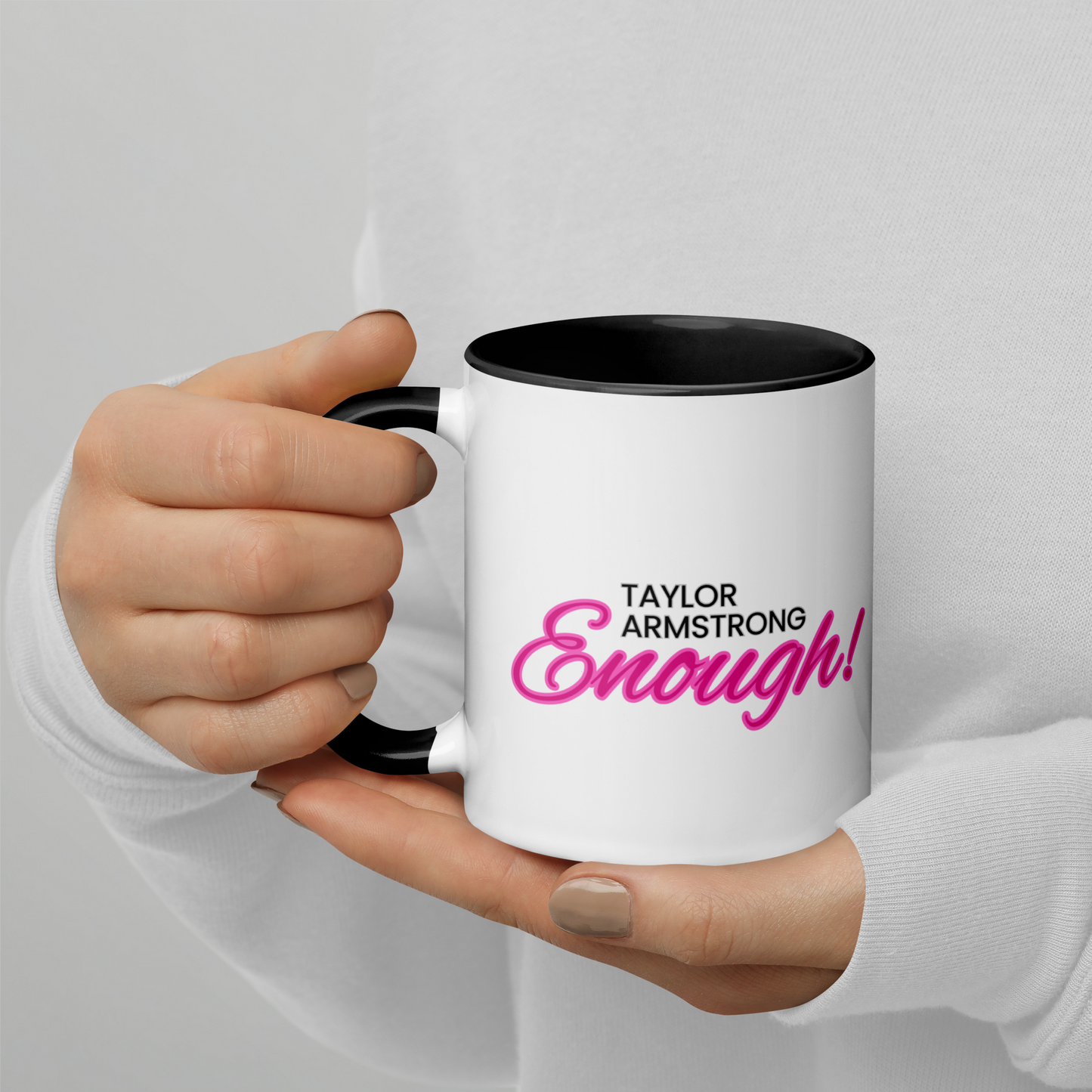 A person holding a white mug with a black handle and black interior with the phrase Taylor Armstrong ENOUGH! written in black and pink font in the center.