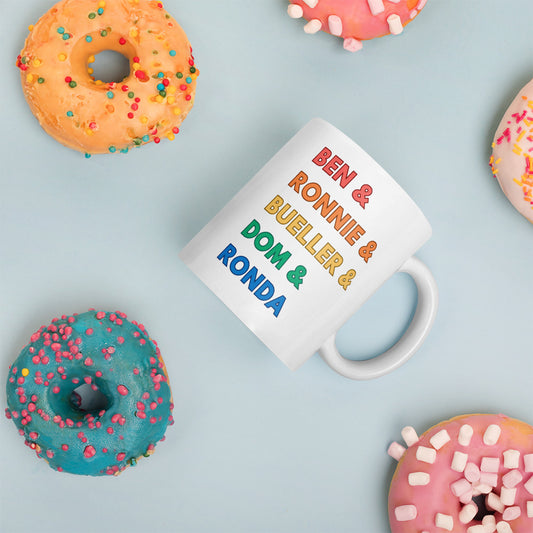 A white mug with "Ben & Ronnie & Bueller & Dom & Ronda" printed in rainbow font surrounded by colorful donuts. 